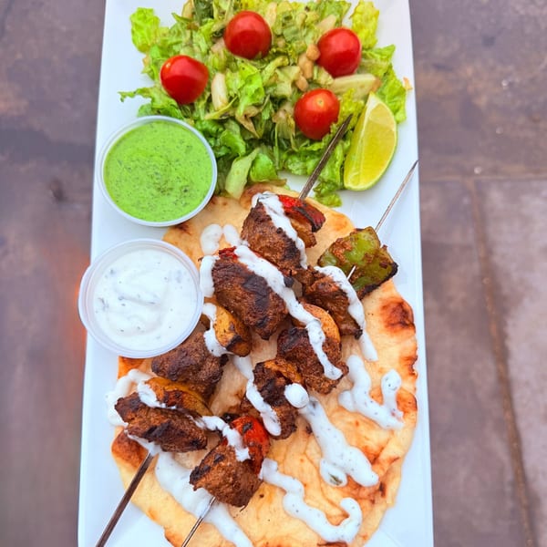 Pines Bar and Grill's chicken skewers with salad, lime, and two dipping sauces on a white plate.
