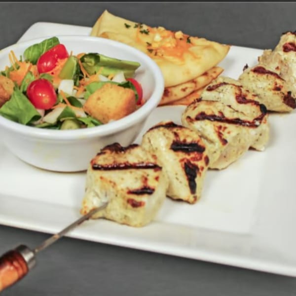 Grilled chicken skewers, a side salad with croutons, and cheesy flatbread on a white plate.
