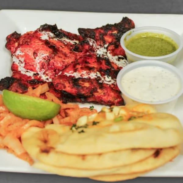 Tandoori chicken with naan, lime, onions, and two dipping sauces on a white plate.