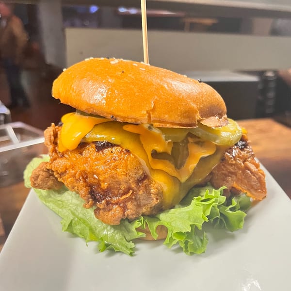 Crispy fried chicken sandwich with melted cheese, pickles, and lettuce on a brioche bun.
