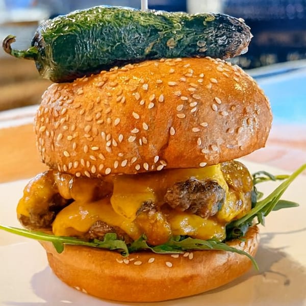 A juicy cheeseburger with melted cheese, arugula, and a roasted jalapeño on top.